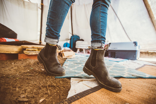 Person wearing black high top blundstone with cuffed blue jeans on a campsite.