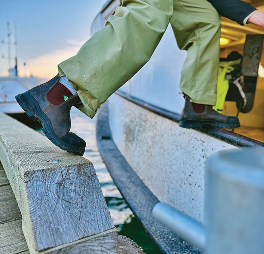 Pair of Blundstone XFR boots in rustic brown worn getting onto a fishing boat.