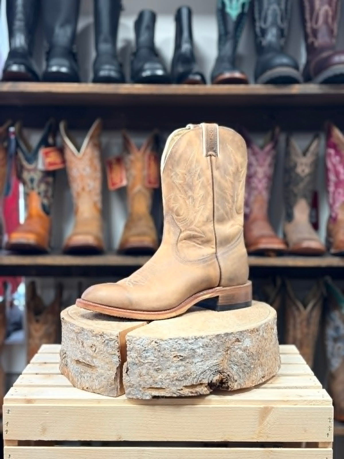 Tan cowboy boot on a wooden block with boots in the background